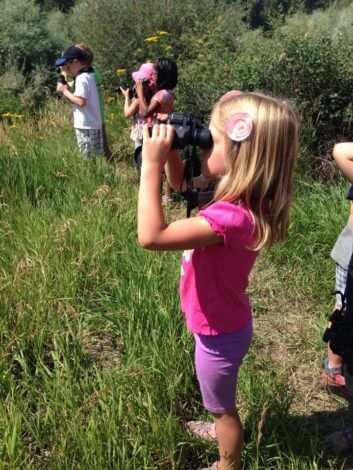 A young summer camper watches birds with her own pair of binoculars!
