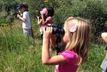 A young summer camper watches birds with her own pair of binoculars!