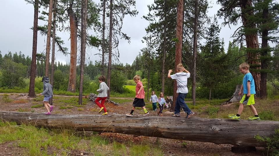 a group of summer campers plays on a fallen log at Camp Paxson in the Seeley Swan Valley