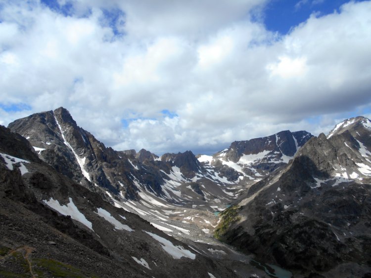 wild mountain peaks in the Beartooth Mountains, with patches of snow, beneath blue skies and puffy clouds