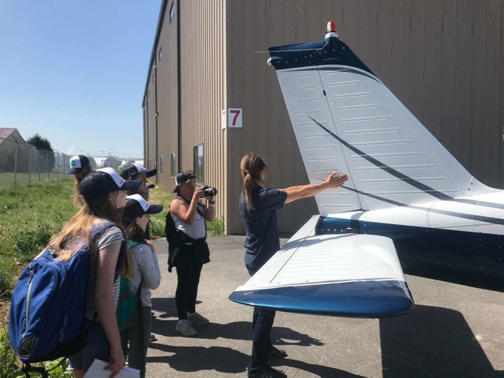 female pilot teaching about the parts of a plane to a group of young women in science camp