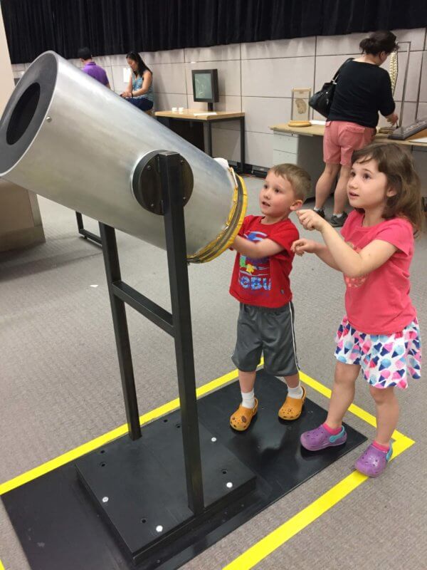 two kids looking through a huge telescope at a science center