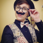 Jessie Smith, artist, wearing glasses, a fake mustache, a vest, and a pink bowtie