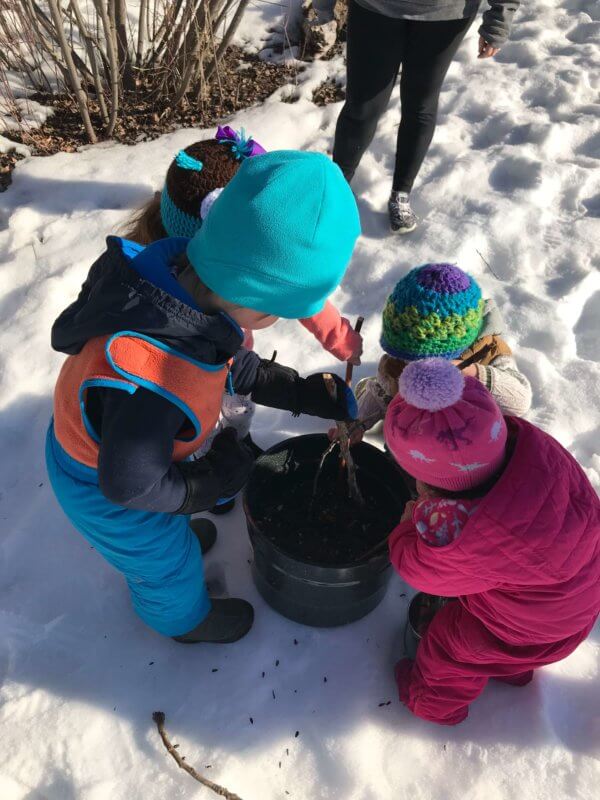 two young children playing in the snow, putting bird seed in a bucket