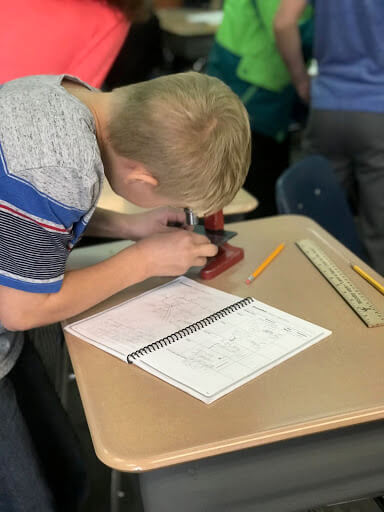 student looking through a microscope and making observations in his nature journal